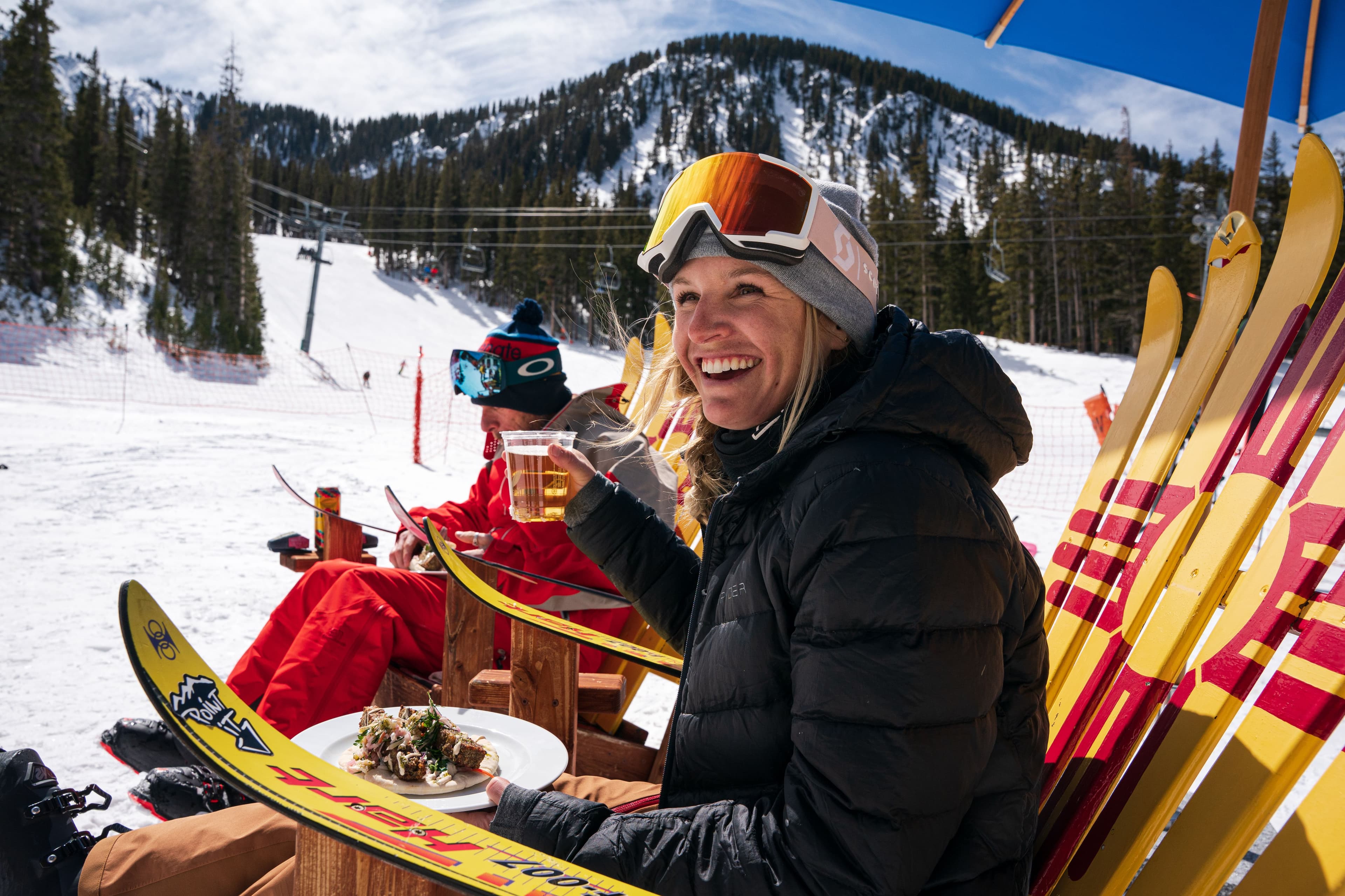 A woman smiling in ski wear with a beer at Whistlestop Cafe.