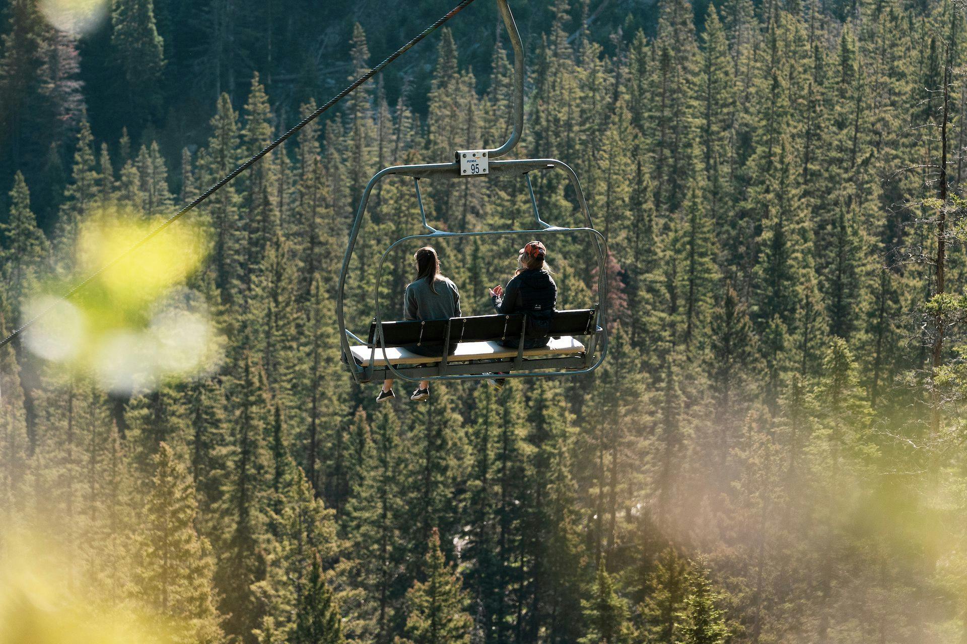Two guests enjoy the view from a scenic lift ride on a sunny summer day at Taco Ski Valley